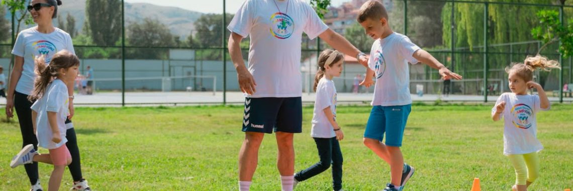 Kids guided by instructors at a park balance on a beam for fun and exercise.