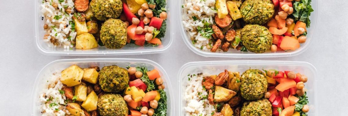 Colorful meal prep containers with falafel, chickpeas, rice, and vegetables for a healthy lifestyle.