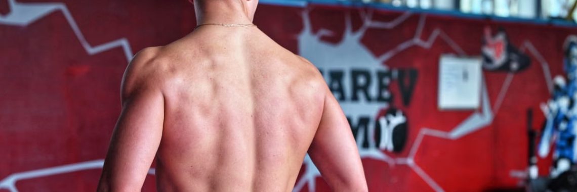 Shirtless man showcasing muscular back indoors in fitness gym.