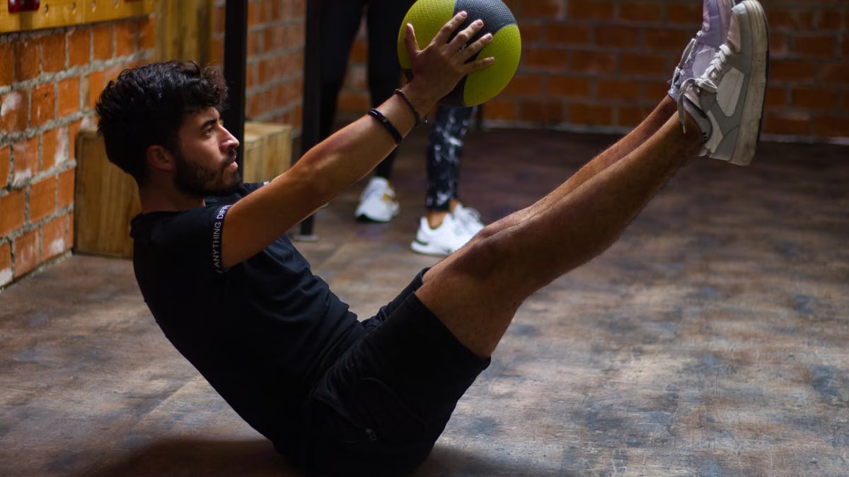 Focused man performing core exercises with a medicine ball in an indoor gym highlighting fitness and strength.